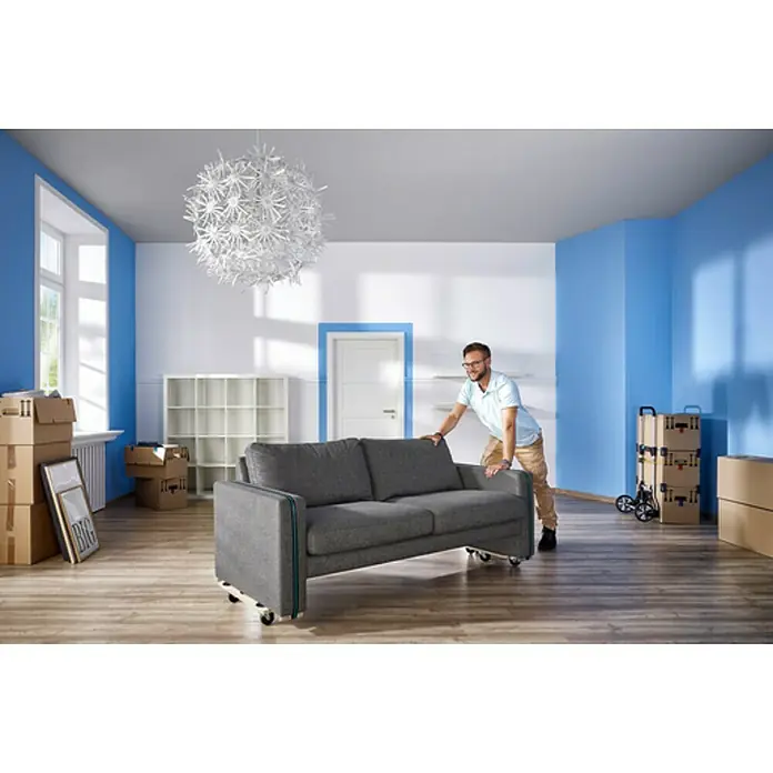 Wolfcraft Base con ruedas FT300 - L x An x Al: 565 x 390 x 120 mm, Capacidad de carga: 200 kg, Madera - Un hombre está empujando un sofá gris con ruedas a través de una habitación. El sofá es el producto principal de la imagen.
