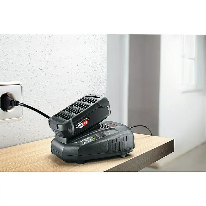 Bosch Power for All 18V Akku PBA 18V 2.5Ah W-B - 18 V, 2,5 Ah - Akku und Ladegerät auf einem Holztisch. Der Akku wird gerade über eine Steckdose geladen.