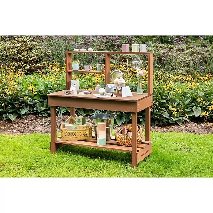 Muddy Buddy Cocina infantil Mud Starter - 80 x 40 x 90 cm, Madera, Marrón - Cocina de barro de madera para niños con fregadero, estantes y accesorios de juego, instalada en un jardín vibrante.