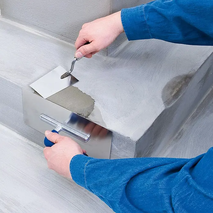 Knauf Reparaturspachtel - 10 kg, Schichtdicke: 3 mm - 50 mm - Anwendung von Mörtel auf Beton mit einer Maurerkelle und einem Spachtel, um eine glatte Oberfläche zu erzielen.