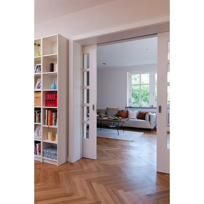 Knauf Bodenausgleichsmasse - 20 kg, Schichtdicke: 5 mm - 25 mm - Helle Wohnung mit Bücherregal und Glasschiebetüren, die einen Blick in ein gemütliches Wohnzimmer mit Holzboden freigeben.