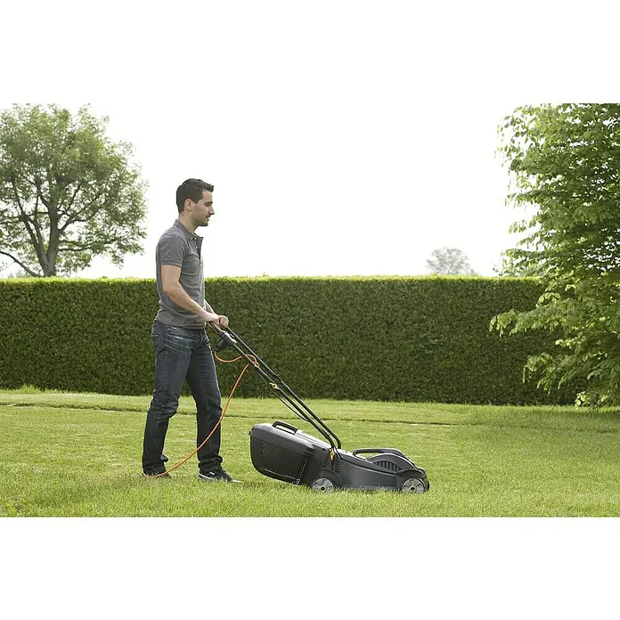 Alpina Cortacésped eléctrico BL320E - 1.000 W, Ancho de corte: 32 cm - Un hombre está cortando el césped con una cortadora de césped en el jardín, con un césped verde y exuberante que ofrece un hermoso telón de fondo.