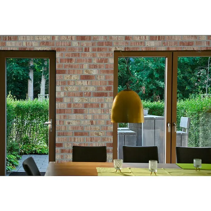 Celina Klinker Verblendstein-Ecke Wasserstrich Auckland - 21,5 cm x 6,5 cm x 15 mm, Beige/Rot, Steinoptik - Ein Innenraum mit einer Ziegelwand, die durch Türen und Fensterblicke in einen üppigen Garten ergänzt wird. Die Ziegel verleihen dem Raum Wärme und Textur.