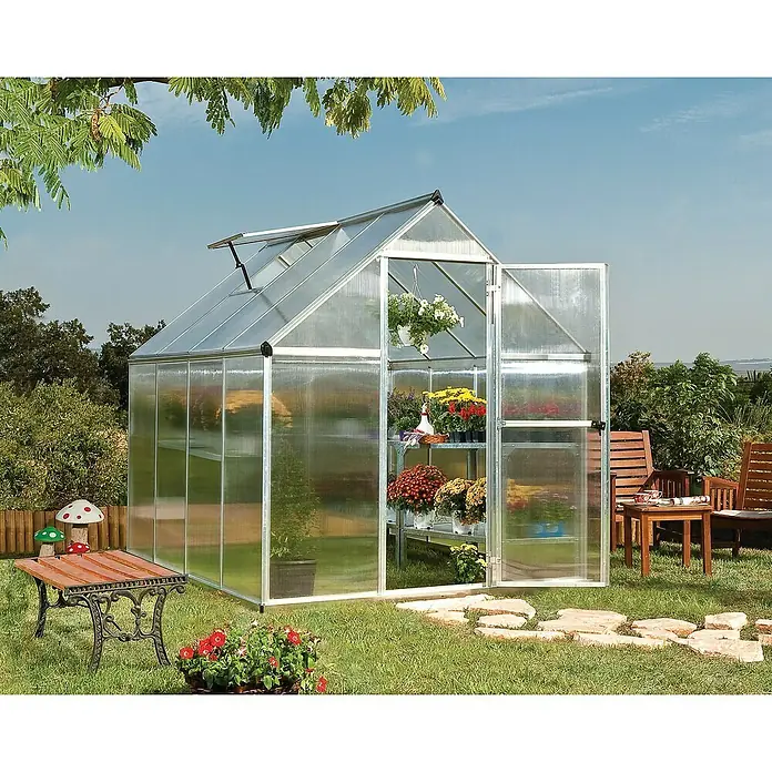 Palram – Canopia Invernadero Mythos - Medidas ext. (An x Pr): 185 x 247 cm, 4 mm, Plateado - Un espacioso invernadero con puertas abiertas, que alberga una variedad de plantas y está rodeado de un jardín bien cuidado.