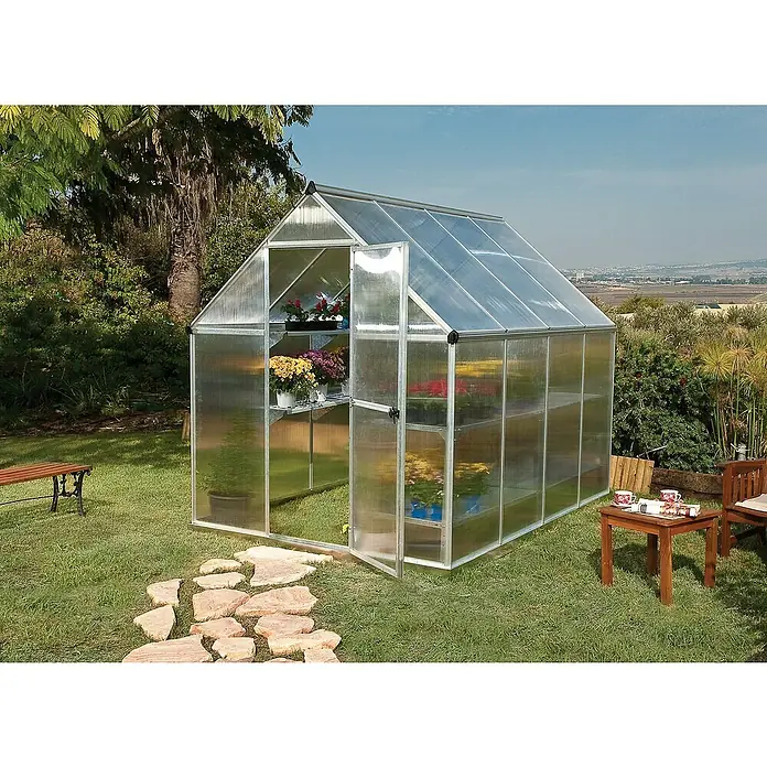 Palram – Canopia Invernadero Mythos - Medidas ext. (An x Pr): 185 x 247 cm, 4 mm, Plateado - Un invernadero con estantes llenos de plantas con flores en un jardín, con un camino de losas y muebles de jardín.