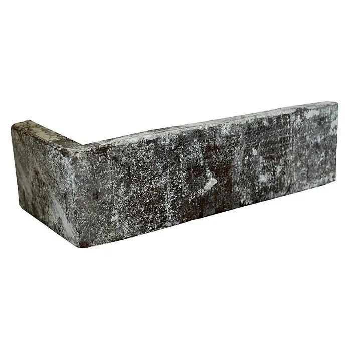 Celina Klinker Verblendstein-Ecke Vintage Sydney - 24 cm x 7,1 cm x 15 mm, Weiß/Braun, Steinoptik - Nahaufnahme eines kantigen, verwitterten Bordsteins auf schwarzem Hintergrund. Das Bauelement zeigt eine robuste Textur.