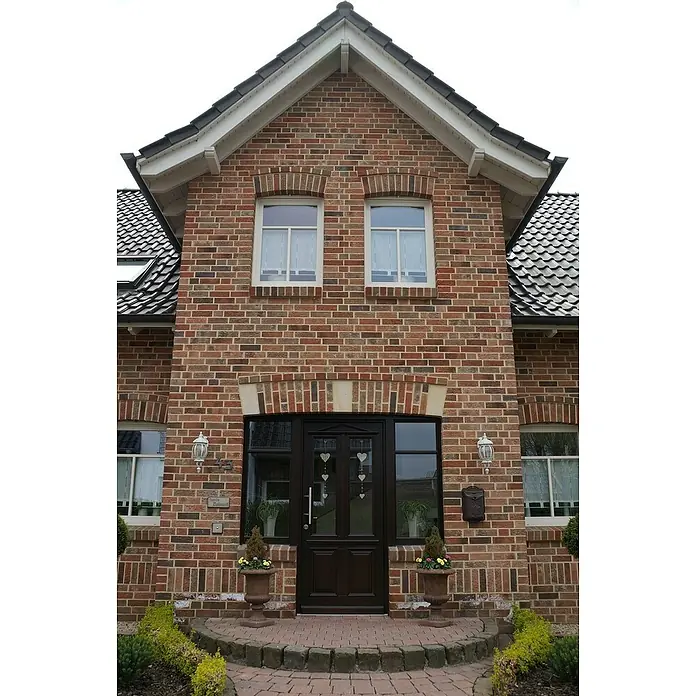 Celina Klinker Verblendstein Montana Gelderland - 7,1 x 24 cm, Braun/Beige, Steinoptik - Fassade eines Backsteinhauses mit einer dunklen Haustür, flankiert von Fenstern und Blumenkübeln, die ein einladendes Entree schaffen.