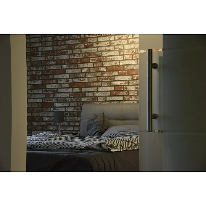 Celina Klinker Verblendstein Vintage Hamburg - 5,2 x 24 cm, Weiß/Rot, Steinoptik - Blick durch eine Tür auf ein Schlafzimmer mit einem Bett vor einer Ziegelwand. Das Bett ist mit gestreifter Bettwäsche versehen.