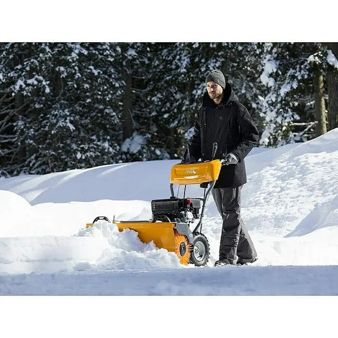 Stiga Kehrmaschine SWS 800 G - 4,4 kW - Ein Mann benutzt eine gelbe Stiga Schneefräse, um einen verschneiten Weg freizumachen. Ideal für Winterarbeiten im Freien.