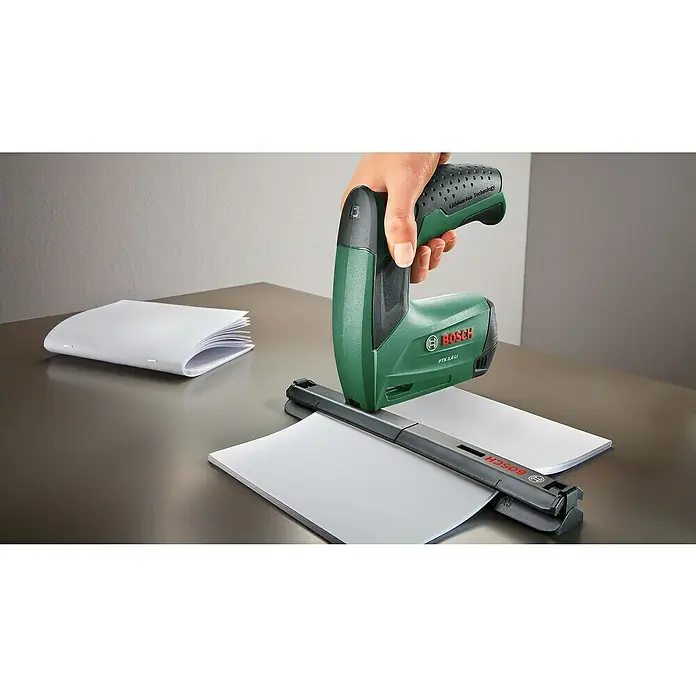 Bosch Akku-Tacker PTK 3,6 LI Office Set - 3,6 V, Klammertiefe: 4 mm - 10 mm - Eine Bosch PTK 3,6 LI Akku-Tackermaschine wird verwendet, um Papier auf einem Schreibtisch zu befestigen, während ein weiteres geheftetes Papier daneben liegt.