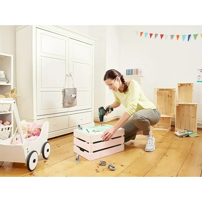 Bosch Power for All 12V Akku-Schlagbohrschrauber EasyImpact 12 - 12 V, 1 Akku, 2 Ah - Eine Frau montiert einen rosa gestrichenen Kasten mit Rollen mit einem Akkuschrauber in einem hellen Raum.