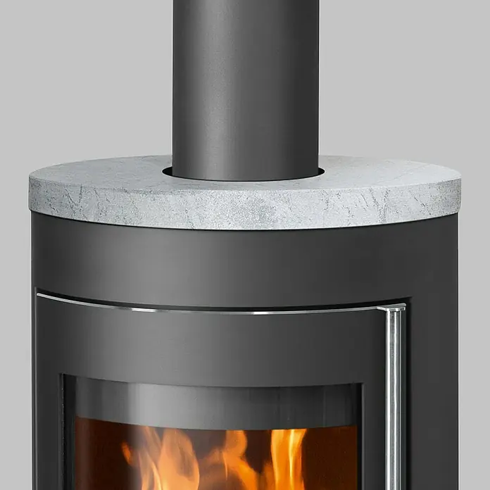 Justus Kaminofen Meva - 5,5 kW, Raumheizvermögen: 88 m³, Farbe Verkleidung: Speckstein, Schwarz - Detailaufnahme eines modernen Kaminofens mit Betonplatte und sichtbarem Feuerraum, der eine angenehme Wärme ausstrahlt.