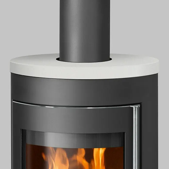 Justus Kaminofen Meva - 5,5 kW, Raumheizvermögen: 88 m³, Farbe Verkleidung: Seidenweiß, Schwarz - Nahaufnahme eines Kaminofens mit weißer Oberseite und dunklem Ofenrohr. Im Inneren brennt ein helles Feuer.