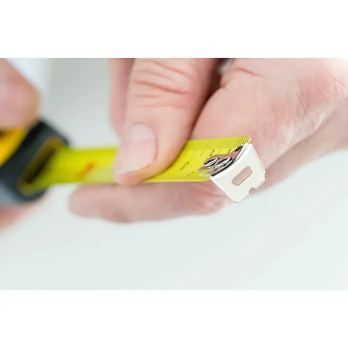 Stanley Cinta métrica extensible BIMATERIA TYLON™ - Largo: 8 m, Plástico - Primer plano de una cinta métrica amarilla sujeta en la mano, destacando la precisión y funcionalidad de esta herramienta esencial.