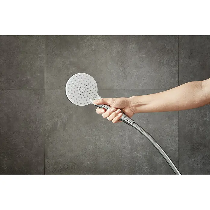 Hansgrohe Crometta Handbrause Vario - Anzahl Funktionen: 2 Stk., Durchmesser: 10 cm, Weiß/Chrom - Nahaufnahme einer Hand, die einen modernen Duschkopf vor einer grauen Wand hält. Der Duschkopf zeichnet sich durch ein elegantes, rundes Design aus.