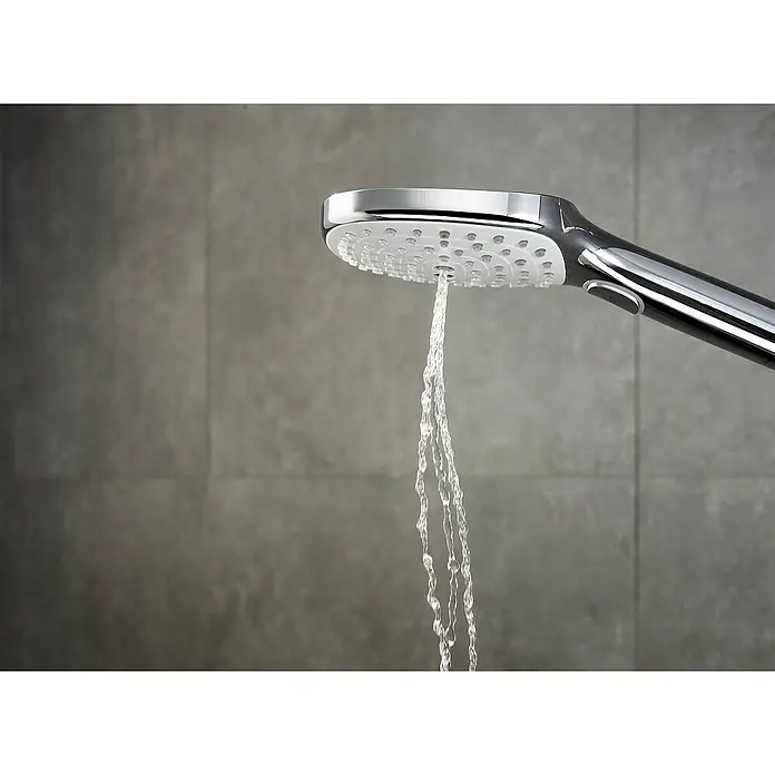 Hansgrohe Handbrause Raindance Select E - Anzahl Funktionen: 3 Stk., Durchmesser: 12 cm, Chrom - Nahaufnahme eines verchromten Duschkopfs, aus dem Wasser fließt, vor einem grauen, gefliesten Hintergrund.