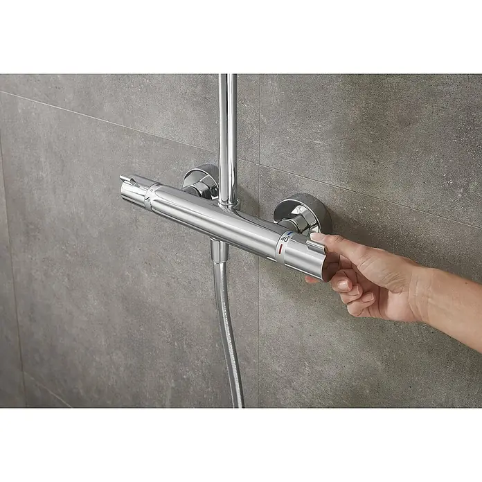 Hansgrohe Duschsystem Croma Showerpipe 160 - Mit Thermostatarmatur, Lochabstand: 93,2 cm, Anzahl Strahlarten: 4 Stk., Chrom, Höhe: 110,1 cm - Hand reguliert die Temperatur an einer glänzenden, verchromten Duscharmatur mit Thermostat vor einer grauen gefliesten Wand.