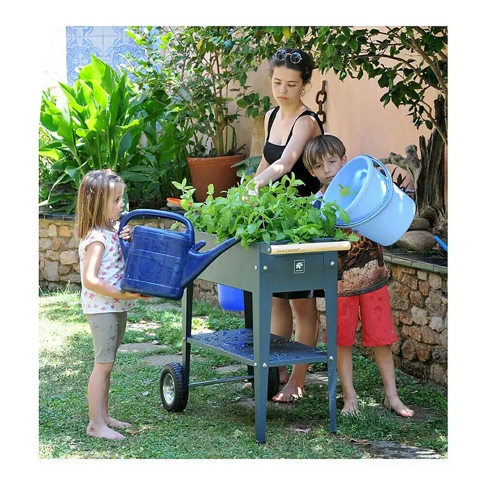 Herstera Garden Kräuterhochbeet Urban - L x B x H: 85 x 50 x 80 cm, Anthrazit - Familie gießt Pflanzen in einem erhöhten Beet auf Rädern. Das graue Beet mit Pflanzfläche ist ideal für Gärten und Terrassen.