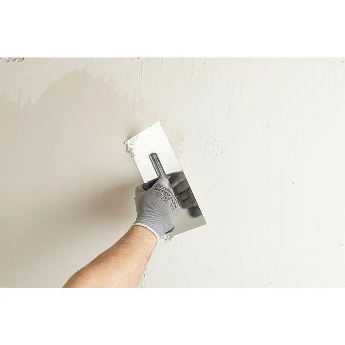 Knauf Rotband Flächenspachtel Plus - 4 kg - Nahaufnahme einer Hand mit einem Spachtel, die Putz auf eine Wand aufträgt, um eine glatte Oberfläche zu schaffen.