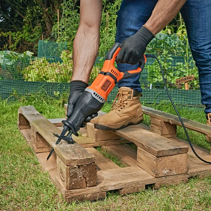 Black+Decker Sierra de sable BES301-QS - 750 W - Un hombre usa una sierra de vaivén Black+Decker para cortar un palé de madera en el exterior. La sierra es naranja y negra y es de alimentación eléctrica.