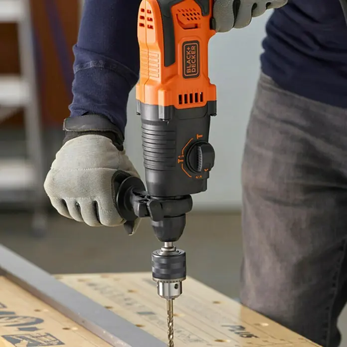 Black+Decker Martillo combinado BEHS01K-QS - 650 W, 1,4 J, Alojamiento SDS-Plus - Primer plano de un taladro Black+Decker en acción, sostenido por una persona con guantes de trabajo, para proyectos de bricolaje.