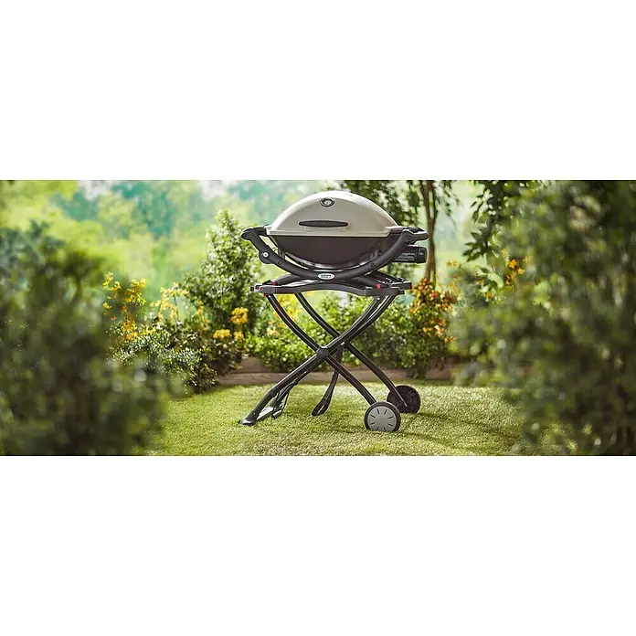 Weber Carro con ruedas para barbacoa - Específico para: Serie de barbacoa Q1000 / Q2000 - Una barbacoa de gas Weber Q 1200 con tapa gris y base negra reposa sobre un carro negro con ruedas en un espacio verde al aire libre.