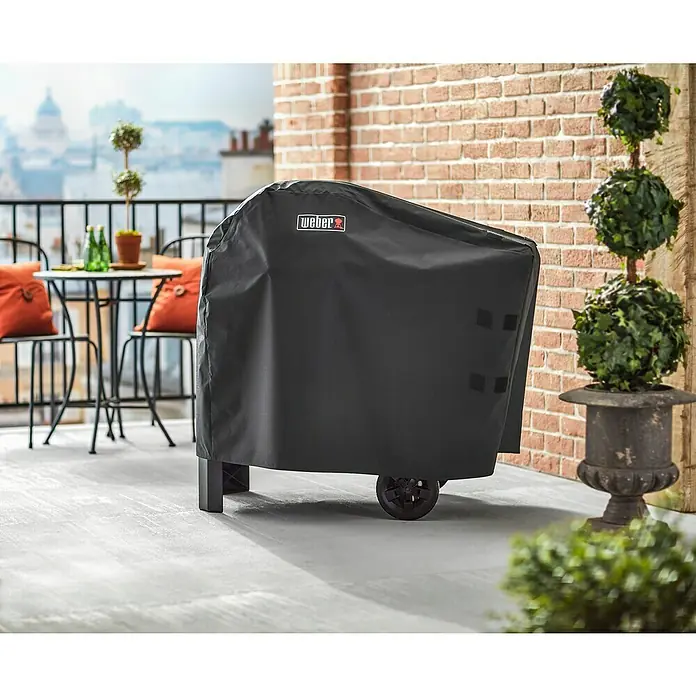 Weber Premium Grill-Schutzhülle - Passend für: Weber Pulse 1000/2000 mit Rollwagen - Weber Grill mit schwarzer Abdeckung auf einer Terrasse mit Blick auf eine Stadt im Hintergrund.