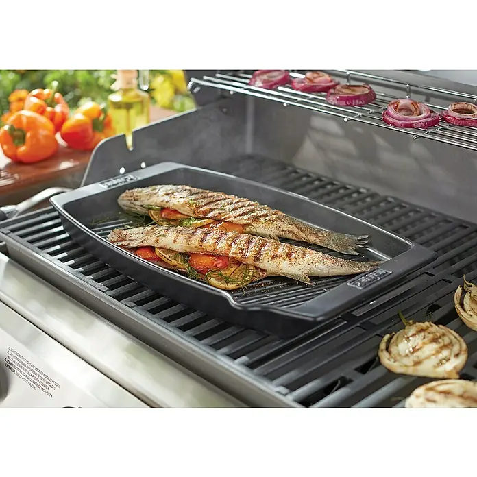 Weber Grillpfanne BBQ Keramik - L x B: 47 x 28 cm, Höhe: 4,4 cm - Gegrillter Fisch mit Gemüse in einer schwarzen Grillpfanne auf einem Weber Grill, dazu Zwiebeln und Paprika.