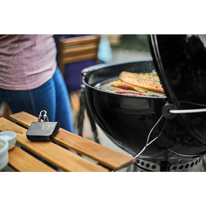 Weber Smart-Grill-Assistent - L x B x H: 9,8 x 3,4 x 7,5 cm - Ein Grillthermometer zeigt die Temperatur von 63 Grad an, während daneben der Grill mit Fisch und Fleisch befeuert wird.