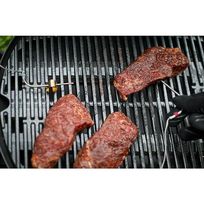 Weber Smart-Grill-Assistent - L x B x H: 9,8 x 3,4 x 7,5 cm - Drei Steaks werden auf einem Grill zubereitet, wobei die Temperatur mit einem Thermometer überwacht wird, um die Garstufe zu prüfen.