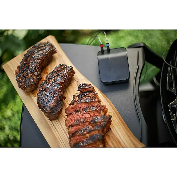 Weber Smart-Grill-Assistent - L x B x H: 9,8 x 3,4 x 7,5 cm - Saftige Steaks, perfekt gegrillt und auf einem Holzbrett angerichtet, neben einem smarten Fleischthermometer.