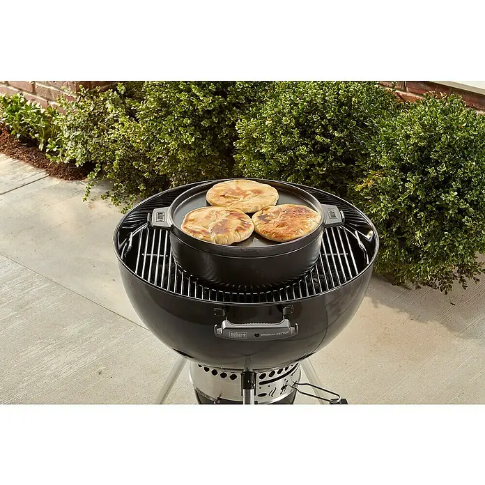 Weber Dutch Oven 2in1 - L x B x H: 33,5 x 42,37 x 12,27 cm, Gusseisen - Ein Weber Kugelgrill mit einem schwarzen Kochtopf mit drei Fladenbroten darauf, im Freien.