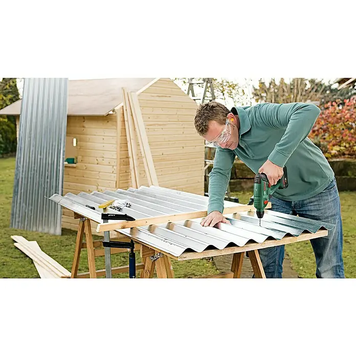 Bosch Power for All 18V Akku-Bohrhammer Uneo Maxx - 18 V, 1 Akku, 0,6 J - Ein Handwerker befestigt mit einer grünen Bohrmaschine eine gewellte Metallplatte, wobei er Schutzbrille und Ohrenschützer trägt, um sich zu schützen.