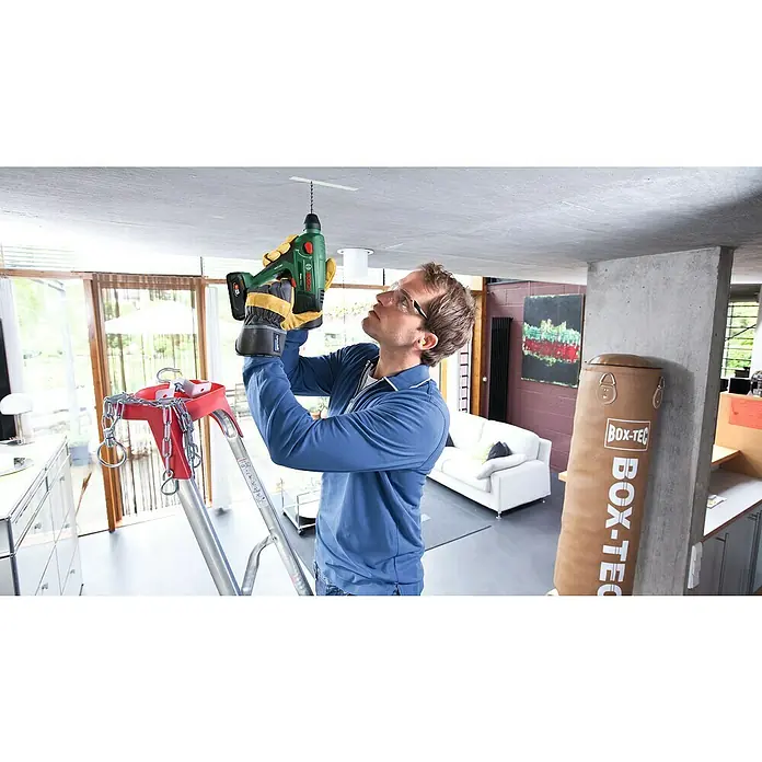 Bosch Power for All 18V Akku-Bohrhammer Uneo Maxx - 18 V, 2 Akkus, 0,6 J - Ein Mann bohrt mit einer Bosch-Bohrmaschine ein Loch in die Decke, während er auf einer Leiter steht.