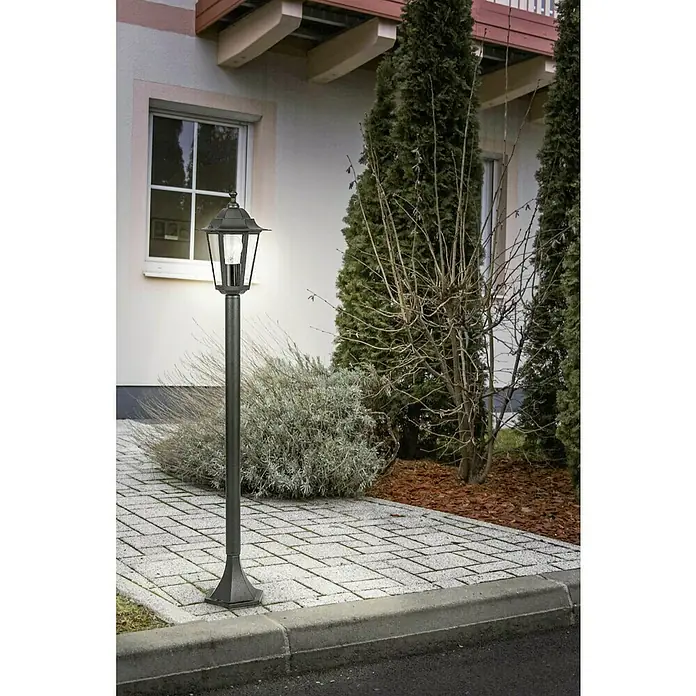Eglo Laterna 4 Außenleuchte - 60 W, Farbe Gehäuse: Schwarz, 20,5 x 100 cm, Ohne Leuchtmittel - Eine stilvolle, schwarze Gartenlaterne beleuchtet einen gepflasterten Weg vor einem Haus, umgeben von üppiger Vegetation und Bäumen.