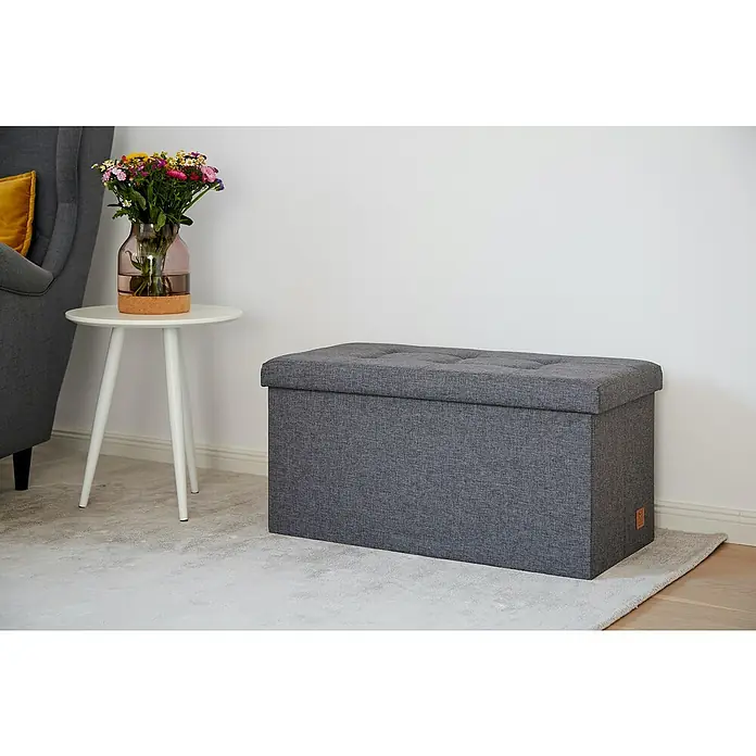 Store It Premium Sitz- & Aufbewahrungsbox Home - L x B x H: 38 x 76 x 38 cm, Grau - Grauer, rechteckiger Polsterhocker mit Knopfheftung, der zusätzlichen Stauraum bietet, auf einem hellen Teppich vor einer weißen Wand.