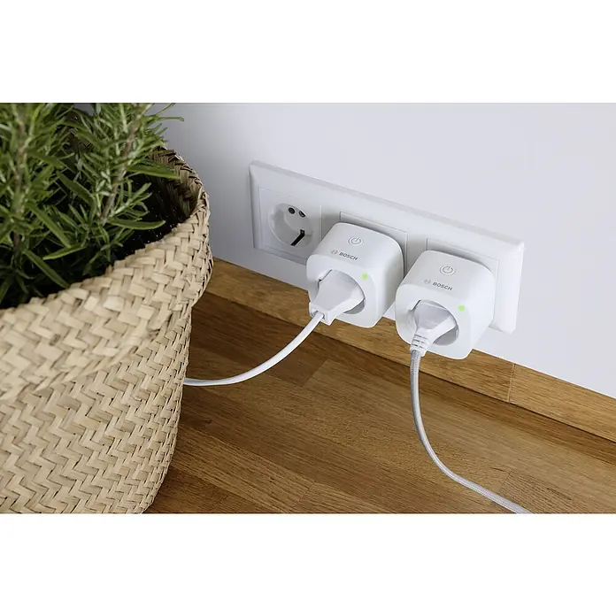 Bosch Smart Home Smart-Steckdose Kompakt - Weiß, Max. Anschlussleistung: 3.680 W - Intelligente Bosch-Steckdosen in einer Steckdosenleiste mit Topfpflanze auf einem Holztisch.