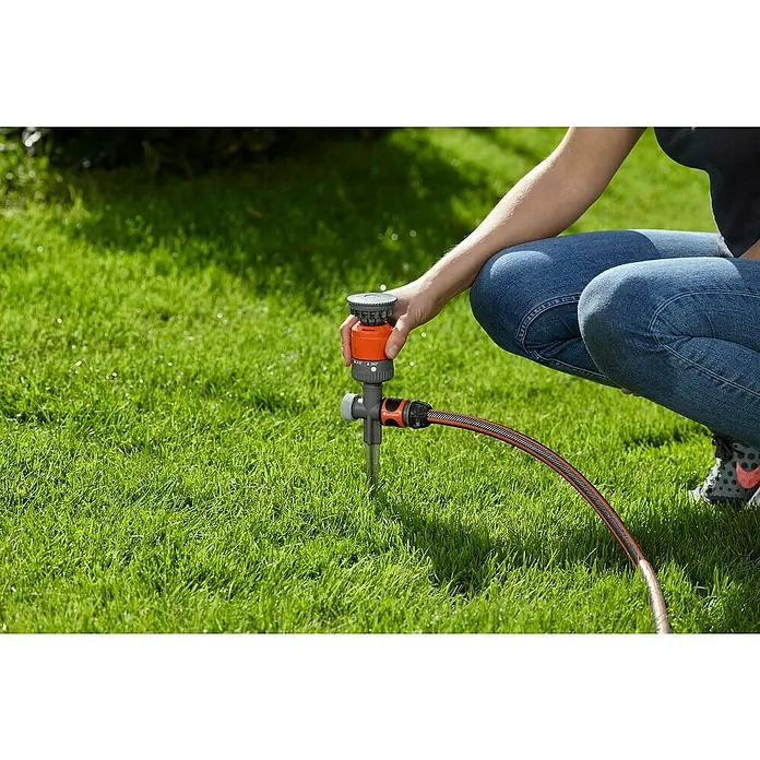 Gardena Comfort Aspersor circular plástico - Estaca, Superficie de rociador máx.: 225 m² - Primer plano de una persona configurando un aspersor multisuperficie Gardena Vario en un césped, centrado en ajustes de riego precisos.
