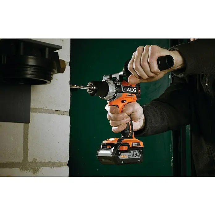 AEG Pro 18V Akku-Schlagbohrschrauber BSB18 C2 BL - 18 V, 1 Akku, 4 Ah, 65 Nm - Nahaufnahme einer AEG Akku-Bohrmaschine beim Bohren in eine Wand, gehalten von einer Person. Die Bohrmaschine ist orange-schwarz mit einem Akku.