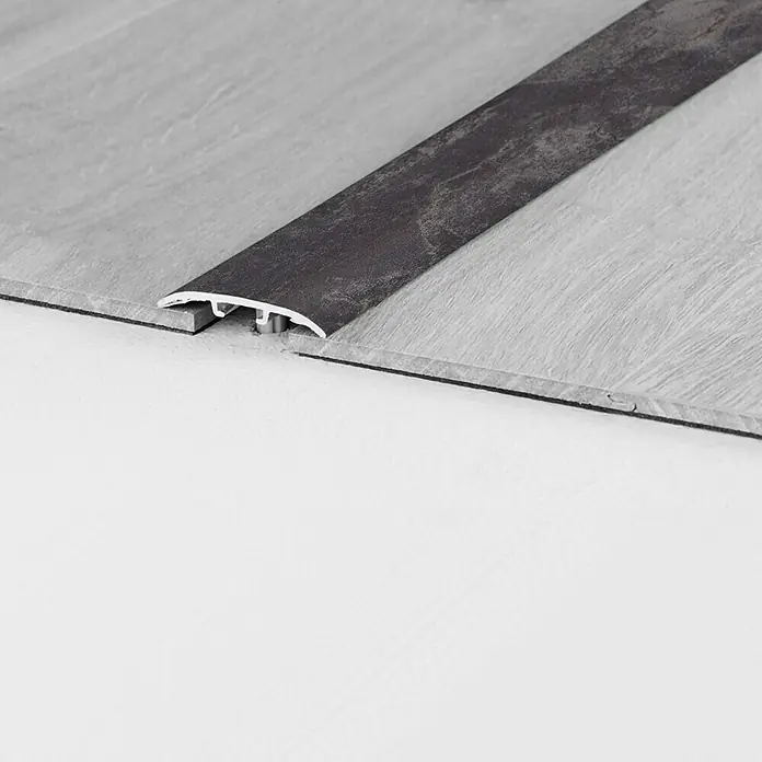 LOGOCLIC Universalprofil 3in1 Deep Blue - L x B x H: 0,9 m x 37 mm x 4,5 mm, Montageart: Schrauben - Detailaufnahme einer grauen Übergangsschiene zwischen zwei Bodenbelägen. Die Schiene ist dunkelgrau und verbindet zwei helle Bodenflächen.