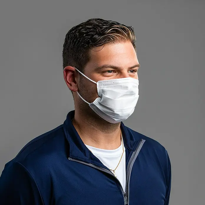 Medizinische Maske weiß - 50 Stk. - Ein Mann mit einem Mundschutz. Der weiße Mundschutz bedeckt Mund und Nase. Er ist mit Gummibändern an den Ohren befestigt.