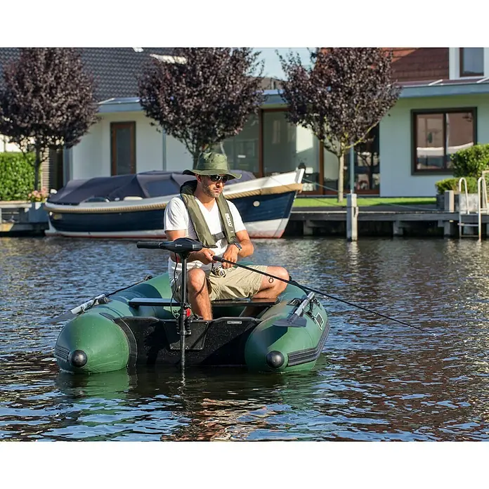 Talamex Motor fueraborda eléctrico TM 66 - 0,14 kW - 0,66 kW, Control de timón, Longitud del eje: 910 mm - Un hombre pesca desde un bote inflable verde en aguas tranquilas. El bote está equipado con un motor para facilitar la navegación.