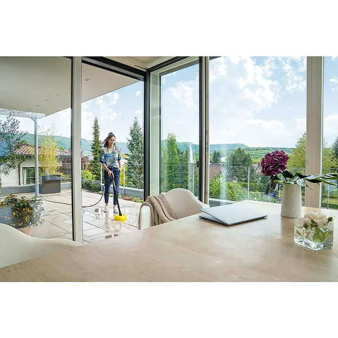 Kärcher Hochdruckreiniger K 2 Power Control Home - 1.400 W, Max. Druck: 110 bar, Fördermenge: 360 l/h - Frau reinigt Außenterrasse mit Kärcher Flächenreiniger. Der Flächenreiniger ist gelb und mit einer Spritzschutzhaube ausgestattet.