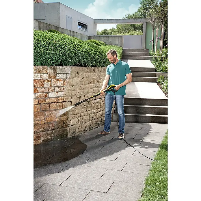 Kärcher Hidrolimpiadora de alta presión K4 Power Control - 130 bar, 1.800 W, Capacidad de bombeo: 420 l/h - Un hombre usa una hidrolimpiadora Kärcher para limpiar una pared de piedra. El resultado es inmediatamente visible.