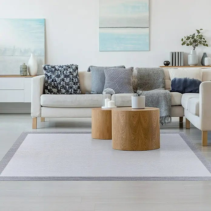 Alfombra de vinilo Living - Gris, 150 x 80 cm - Una alfombra clara con borde gris se coloca en una sala de estar elegante con muebles modernos.