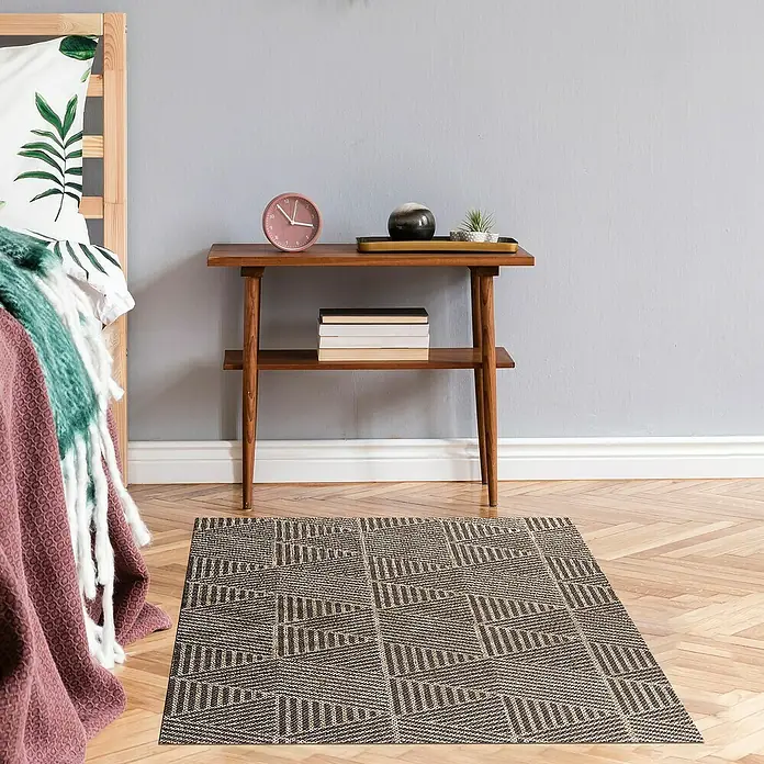 Alfombra de vinilo Living Geométrica - Beige/Marrón, 290 x 200 cm - Una alfombra rectangular con un patrón triangular geométrico en tonos marrones y beige colocada debajo de una mesa de madera junto a una cama.