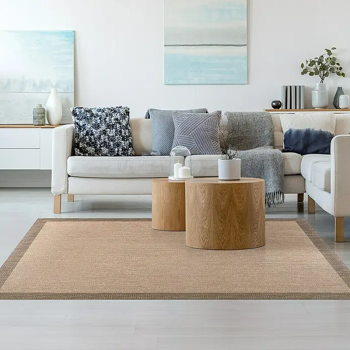 Alfombra de vinilo Living - Beige/Tostado, 90 x 60 cm - Alfombra beige con borde marrón en una sala de estar con sofá, mesas de madera y cuadros abstractos para un ambiente acogedor.
