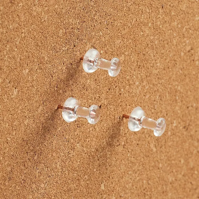 Pinnwandstift - Transparent/Rosegold, Gesamtstückzahl: 25 - Nahaufnahme von drei Reißzwecken mit transparenten Kunststoffköpfen, die in eine Korkwand gesteckt sind.