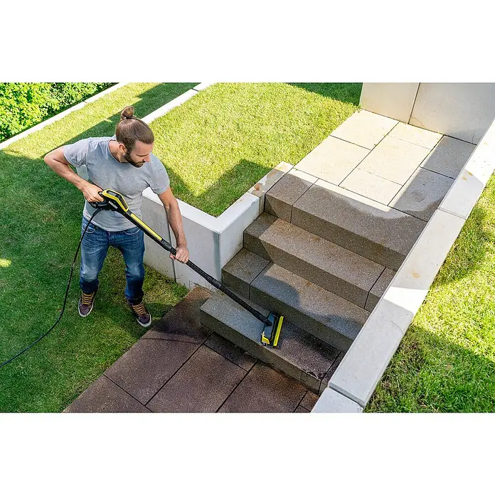 Kärcher Flächenreiniger Powerschrubber PS30 Plus - Passend für: Kärcher Hochdruckreiniger K2 - K7 - Mann reinigt Außentreppe mit einem gelben Kärcher Flächenreiniger, umgeben von Rasen und Betonbegrenzungen, für eine saubere und gepflegte Umgebung.