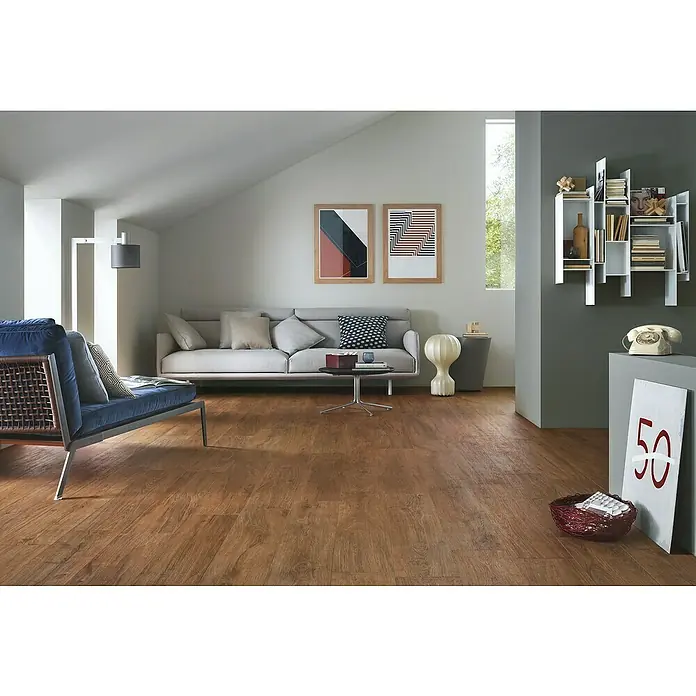 Harmonie by Palazzo Feinsteinzeugfliese - 30 x 120 cm, Eiche Dunkel, Matt - Wohnzimmer mit hellgrauem Sofa, blauem Sessel und Holzboden. Die Wanddekoration umfasst zwei gerahmte Kunstdrucke und ein Bücherregal.